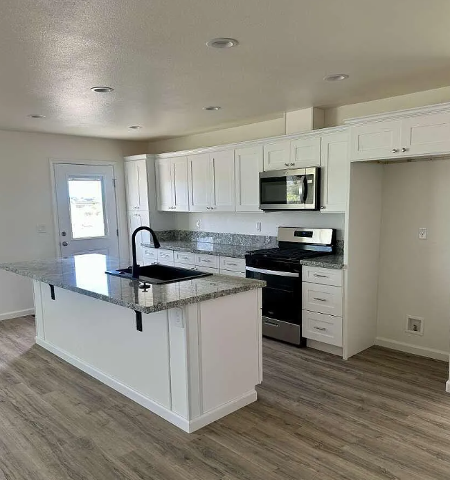 Kitchen finish reference with white shaker cabinetry, granite countertops, black faucet, stainless appliances, island, and LVP flooring